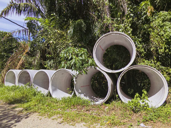 Yığılmış beton drenaj boruları yemyeşil bir tropikal arazide oturur ve yerel altyapı veya su yönetimi için kurulumu bekler..