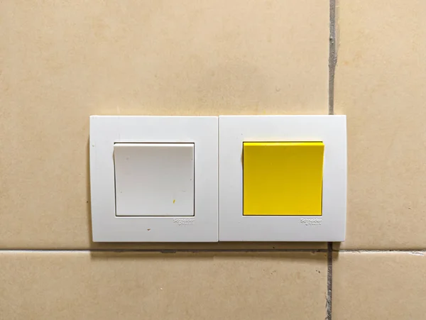 İki tane duvara monte edilmiş ışık anahtarı, biri beyaz ve biri parlak sarı, bronzlaşmış bir duvara karşı beyaz çerçeveye yerleştirilmiş. Temiz ve modern.