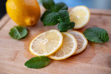 Dilimlenmiş sarı bir limonun yakın çekimi ahşap bir tahtanın üzerinde yatıyor. Taze yeşil nane yaprakları limonun yanında yatıyor..