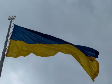 Bulutlu gökyüzüne karşı rüzgarda dalgalanan üç dişli amblemli Ukrayna bayrağı özgürlüğü, dayanıklılığı, birliği ve milli gururu simgeliyor..