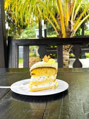 Beyaz bir tabakta beyaz çatalla kaplanmış, krema dolgulu katmanlı sünger keki, sarı şekerleme, şekerleme ve meyve garnitürü, ahşap bir masa üzerine kurulmuş..