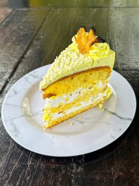 Beyaz bir tabakta beyaz çatalla kaplanmış, krema dolgulu katmanlı sünger keki, sarı şekerleme, şekerleme ve meyve garnitürü, ahşap bir masa üzerine kurulmuş..