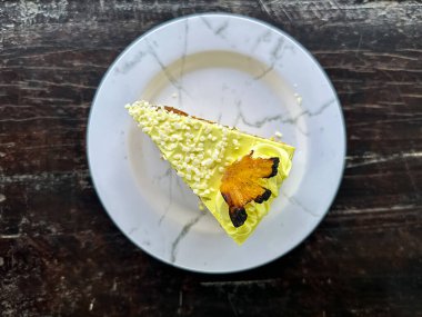 Beyaz bir tabakta beyaz çatalla kaplanmış, krema dolgulu katmanlı sünger keki, sarı şekerleme, şekerleme ve meyve garnitürü, ahşap bir masa üzerine kurulmuş..