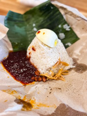Klasik Malezya Nasi Lemak muz yaprağı ve balmumu kağıdında sunuluyor, içinde hindistan cevizi pilavı, sambal, haşlanmış yumurta, kızarmış ançüez ve kavrulmuş fıstık bulunuyor..