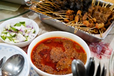 Bir kase kırmızımsı portakal sosuyla servis edilen çeşitli ızgara satay şiş ile dolu metal bir tepsi..