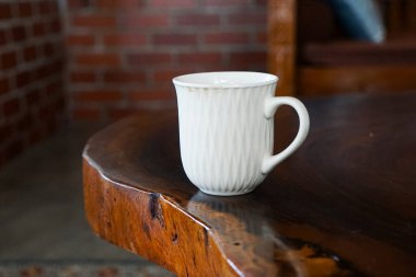 Beyaz seramik kupa, doğal kenarı olan parlak ahşap bir masaya yerleştirilmiş dalgalı desenli bir yüzey..