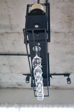 Siyah metal çerçeveli modern tavan ışığı ve altı baş aşağı şarap kadehi, şık bir bar veya mutfak dekorasyonu için beton tavana monte edilmiş..