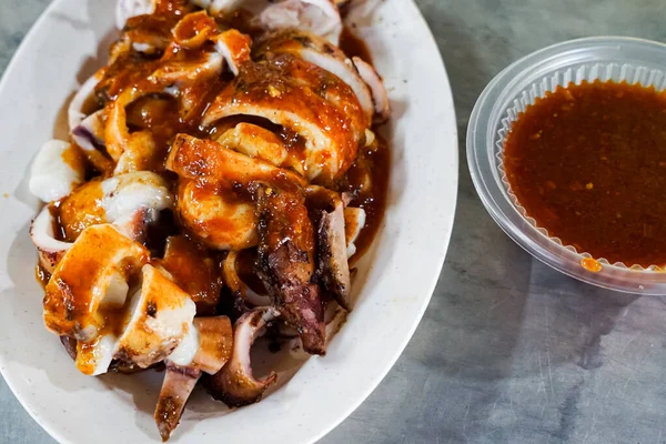 Meşhur bir Malezya deniz ürünleri yemeği olan ızgara doldurulmuş mürekkep balığının yakın çekimi bir paket servis konteynırında servis edildi. Baharat zengini, sulu ve tamamen kömürleşmiş..