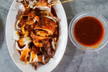 Meşhur bir Malezya deniz ürünleri yemeği olan ızgara doldurulmuş mürekkep balığının yakın çekimi bir paket servis konteynırında servis edildi. Baharat zengini, sulu ve tamamen kömürleşmiş..