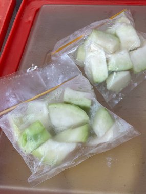 Suya batırılmış yeşil ve beyaz meyve dilimleriyle dolu iki plastik torba, sokak tarzı bir ambalaj metodu sergiliyor..