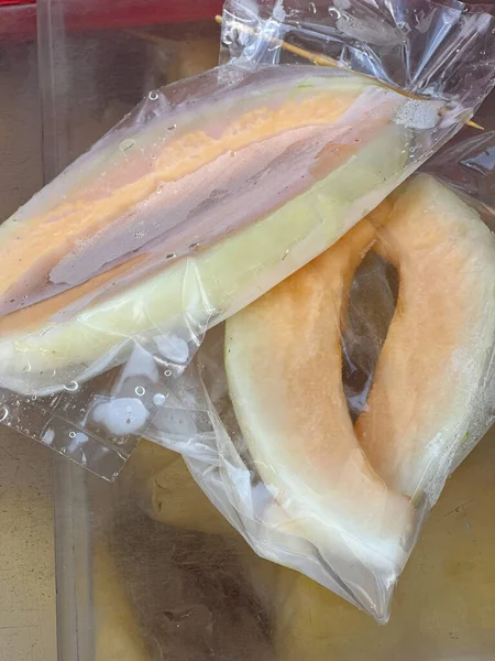 İki taze kavun dilimi temiz plastik poşetlerde, yoğuşma damlacıklarıyla ve hafif atıştırmalıklar için ahşap bir şiş ile mühürlenmiş..