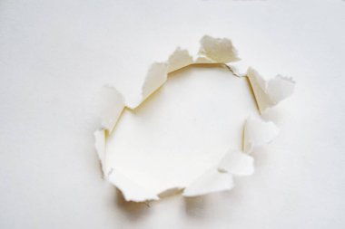 Sivri uçlu dairesel bir deliği olan beyaz bir kağıt parçası temiz beyaz bir arkaplanı ortaya çıkarıyor. Kıvrımlı kenarlar ve kontrastlar, tasarım veya konsept temalar için ideal üç boyutlu görsel efekt oluşturur.