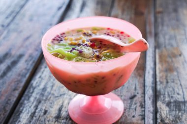 Cendol, kırmızı bir kasede servis edilen bir Malezya tatlısıyla ezilmiş buz, yeşil jöle, kırmızı inciler, hindistan cevizi sütü ve ahşap bir masa üzerinde glutinous pilavı..