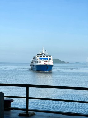 Perlis, Malezya, 3 Aralık 2025: Büyük beyaz ve mavi bir yolcu feribotu açık bir gökyüzünün altında, güvertede ve uzak sularda insanların görebileceği bir rıhtıma yakın..