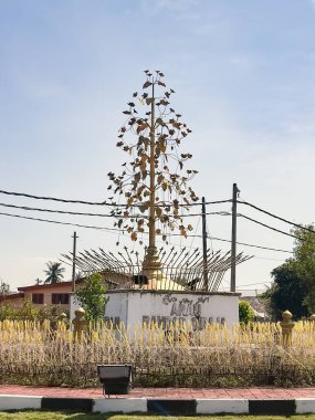 Perlis, Malezya, 4 Aralık 2025: Açık hava kültürel simgesi Arau 'da sembolik mızraklarla çevrili, kaidesi metalik yapraklarla süslenmiş altın seremoni ağacı.