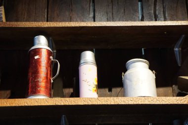 Üç retro içecek kutusu, iki termos ve bir süt kutusu ahşap bir rafta sade ahşap zemin ile düzenlenmiş..