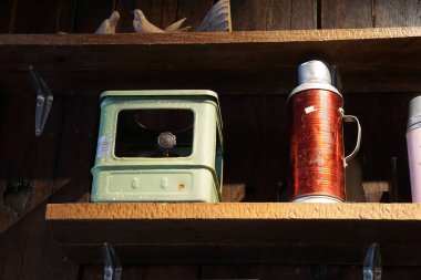 Yeşil metal bir soba, kırmızı termos ve ahşap bir ahşap raftaki ahşap kuş oymalarının nostaljik bir görüntüsü..