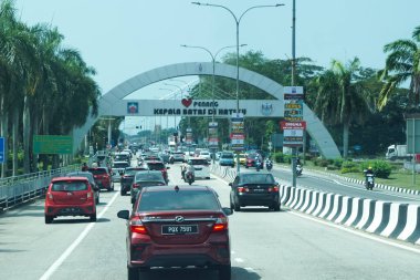 Penang, Malezya, 5 Aralık 2025: Araçlar Kepala Batas 'ta, tropikal ağaçlar ve yol kenarındaki reklamlarla karşılama kemerinin altından geçiyor.