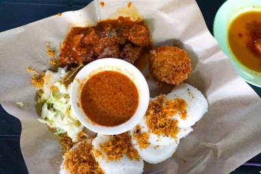 Balmumu kağıtta servis edilen pirinç kekleri, rendang, sebze ve fıstık soslu renkli Longong kertenkele tabağı..