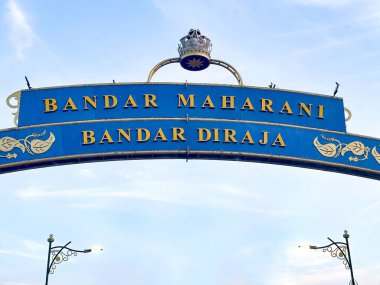 Johor, Malezya, 10 Ocak 2026: Taçlı ve altın harfli dekoratif kemer açık mavi gökyüzü altında 