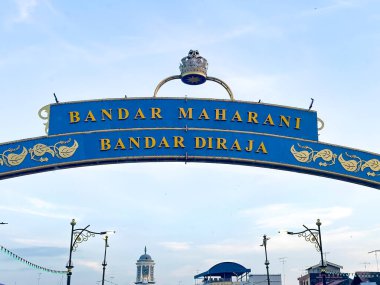 Johor, Malezya, 10 Ocak 2026: Taçlı ve altın harfli dekoratif kemer açık mavi gökyüzü altında 