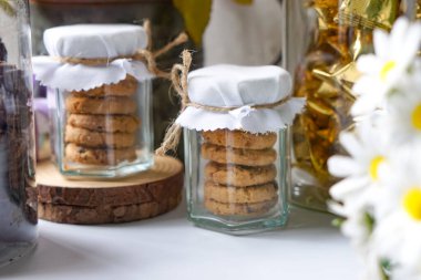 İp yay ve çiçek desenli iki cam kurabiye kavanozu. Hediye vermek ya da sunum yapmak için tasarlanmış..