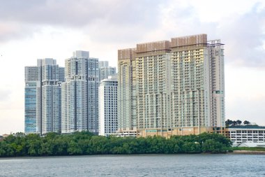 Puteri Limanı, Johor, Malezya 'da deniz kenarında yeşil ve bulutlu gökyüzü olan yüksek binalar kümesi. Johor Boğazından Görünüm.