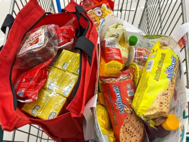 Johor, Malezya, 10 Şubat 2026: Market arabasında çeşitli bakkaliye ve paketlenmiş gıda eşyalarıyla dolu alışveriş poşetleri.