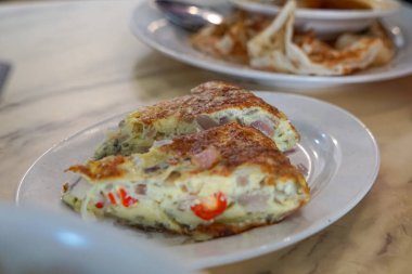 Beyaz tabakta servis edilen sebze ve etle dolu altın omlet..