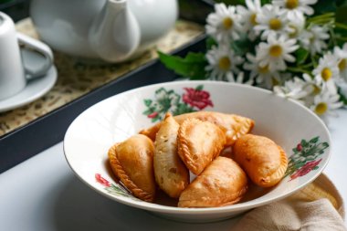 Bir tabak altın körili puf çay seti ve beyaz arka planda papatyalar..