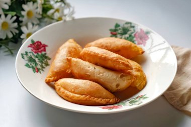 Bir tabak altın körili puf çay seti ve beyaz arka planda papatyalar..