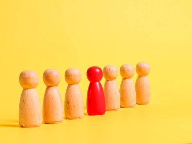 Sarı arka planda nötr figürlerle sırada duran eşsiz kırmızı ahşap figür..