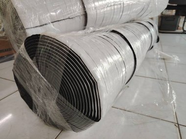 Ağır görev mühürleme ve nefes nefese bırakma uygulamalarında kullanılan beyaz yapışkan kapaklı siyah, kapalı hücre neopren köpük şeritli büyük bir rulo..