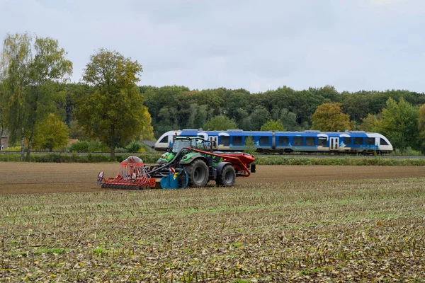 Önünde bir kutu, arkasında bir tohum eken traktör hasat edilmiş bir mısır tarlasında ve arka planda bir tren geçiyordu..
