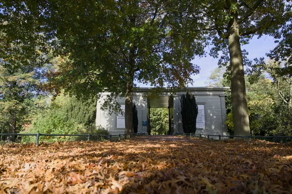 Güneşli bir sonbahar gününde, Zutphen General Mezarlığı 'nın kapısı. Kahverengi yapraklardan oluşan bir halı. Ölümle çok iyi gider ve veda eder.