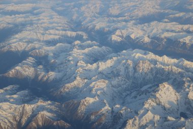 Güneş ışığı ve gölgeli karla kaplı dağ sırasının geniş hava manzarası yüksek irtifa perspektifinden engebeli alp hatlarını ve jeolojik güzelliği ortaya çıkarıyor.