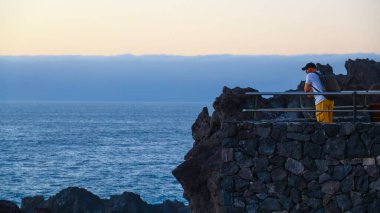 Gün batımında sakin okyanusun yukarısında duran sportif adam Kanarya Adaları 'nın huzurlu ve romantik sahil atmosferini yakalıyor.