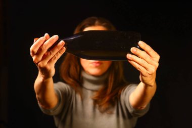 Elinde kameraya doğru uzanan koyu renk bir şarap şişesi tutan kadın, şişe şeklini yakından görüyor, cam yüzeyi ve jest, kutlama, hediye verme, şarap tatma ve kaliteli ürünler için uygun.