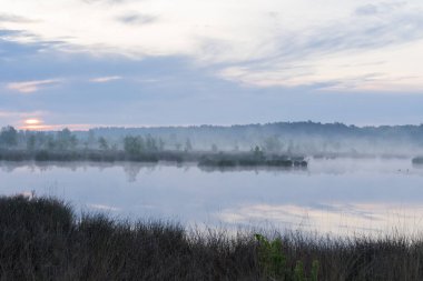 Sabahın erken saatlerinde gökyüzünün yansıması olan bir göl. Gökyüzü bulutlu ve hava serin ve nemli. Sahne sessiz ve huzurlu, göl yalnızlık ve sükunet hissi veriyor. Hollanda 'da Dwingelderveld.