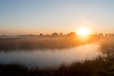 Hollanda 'da bir gölün üzerinde gün doğumu. Gökyüzü turuncu ve güneş ufuktan yükseliyor..