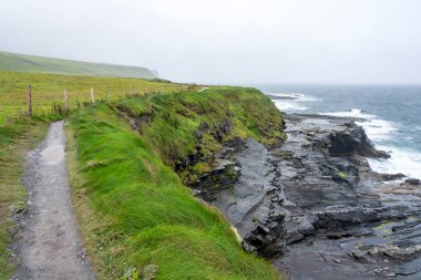 İrlanda 'daki Mohor kayalıklarının panoramik manzarasının yanında engebeli bir Atlantik okyanusu olan küçük bir patika.