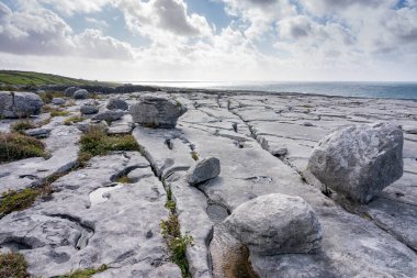 İrlanda 'daki Burren' ler. Mavi gökyüzünün altında bulutlu kayalık bir manzara. Arka planda Atlantik Okyanusu.