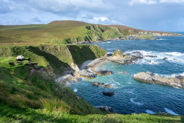 İrlanda 'daki Cleggans Kayalıkları' nın panoramik manzarası. Dalgalı Atlantik Okyanusu ve sağ tarafında koyunlar var..