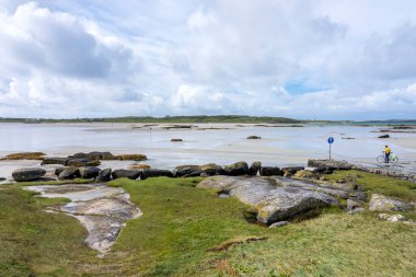 İrlanda 'da deniz kenarında bir plajda bisikletinin yanında bir kişi. Omney Adası 'na gelgit yolu