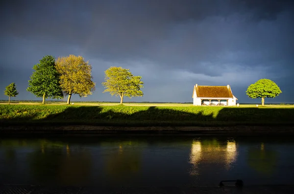 Güneşli beyaz kulübe ve ağaçlar St. Valery-sur-Somme, Fransa 'da karanlık fırtına bulutlarına karşı parlayarak dramatik ve yüksek kontrastlı bir manzara yaratıyor..