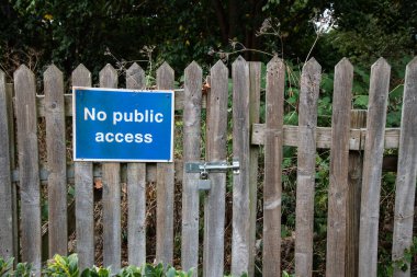 Arkasında ağaçlar ve çalılar olan kilitli bir ahşap kapı ve çitte halka açık erişim işareti yok. Kısıtlı giriş, kırsal alanda özel mülk kavramı.