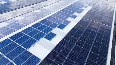 Endüstriyel parktaki bir deponun çatısına kurulmuş güneş panellerinin insansız hava aracı görüntüsü yenilenebilir enerji ve sürdürülebilir enerji üretimi gösteriyor.