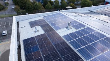 Endüstriyel parktaki bir deponun çatısına kurulmuş güneş panellerinin insansız hava aracı görüntüsü yenilenebilir enerji ve sürdürülebilir enerji üretimi gösteriyor.