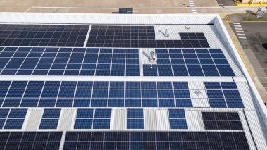 Endüstriyel parktaki bir deponun çatısına kurulmuş güneş panellerinin insansız hava aracı görüntüsü yenilenebilir enerji ve sürdürülebilir enerji üretimi gösteriyor.