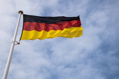 Almanya 'yı, birliği ve ulusal gururu simgeleyen açık gökyüzü, siyah, kırmızı ve altın çizgilere karşı rüzgarda dalgalanan Alman ulusal bayrağı.